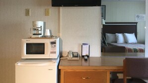 Ett hotellrum med en säng, ett skrivbord med en mikrovågsugn, en kaffebryggare och en tv på väggen.