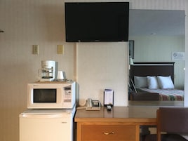 Quarto de hotel com cama, escrivaninha com micro-ondas, cafeteira e televisão na parede.
