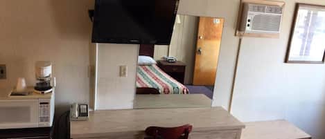 Habitación de hotel con cama, televisor montado en la pared, microondas, cafetera y una silla.