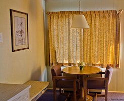 Um quarto com uma mesa redonda de madeira, duas cadeiras, um candeeiro suspenso e uma janela com cortinas.