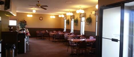 A restaurant with multiple tables and chairs, ceiling fans, and wall-mounted lights.