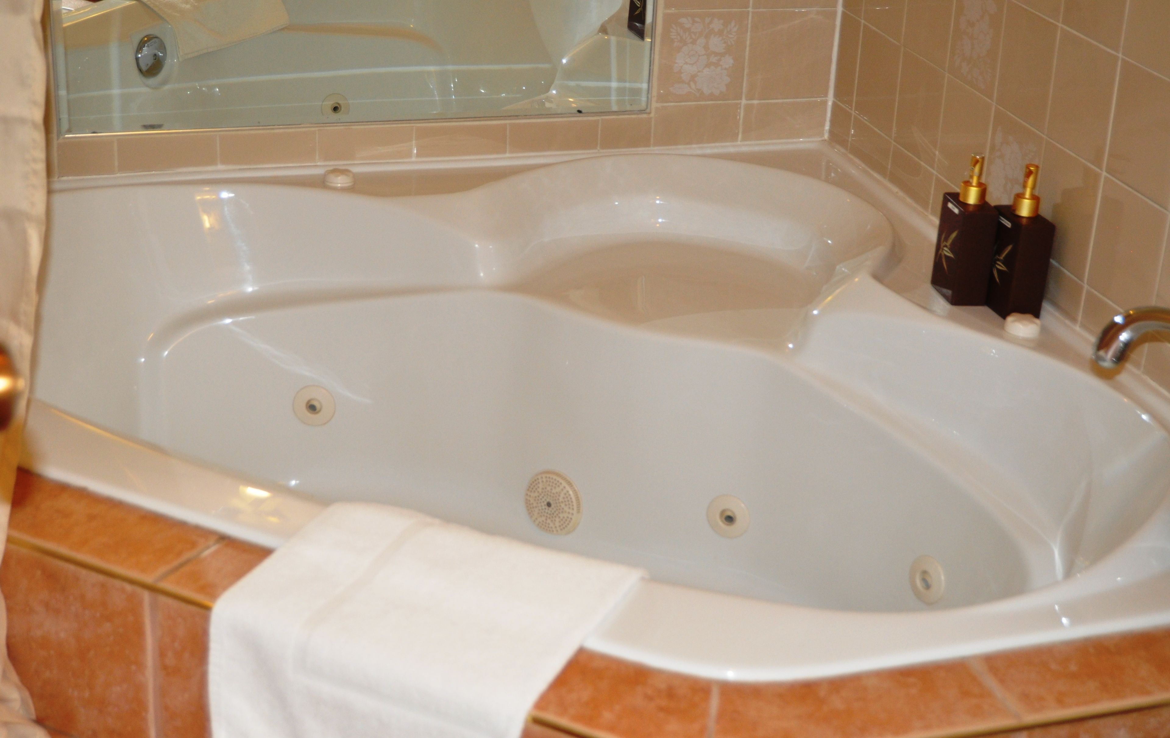 A large, white, freestanding bathtub with a built-in seat, a towel, and two bottles of shampoo.