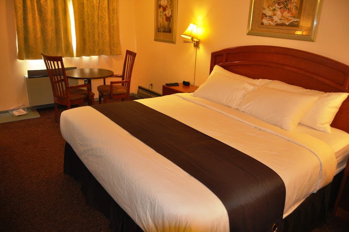 A hotel room with a large bed, a desk, a chair, and a lamp.