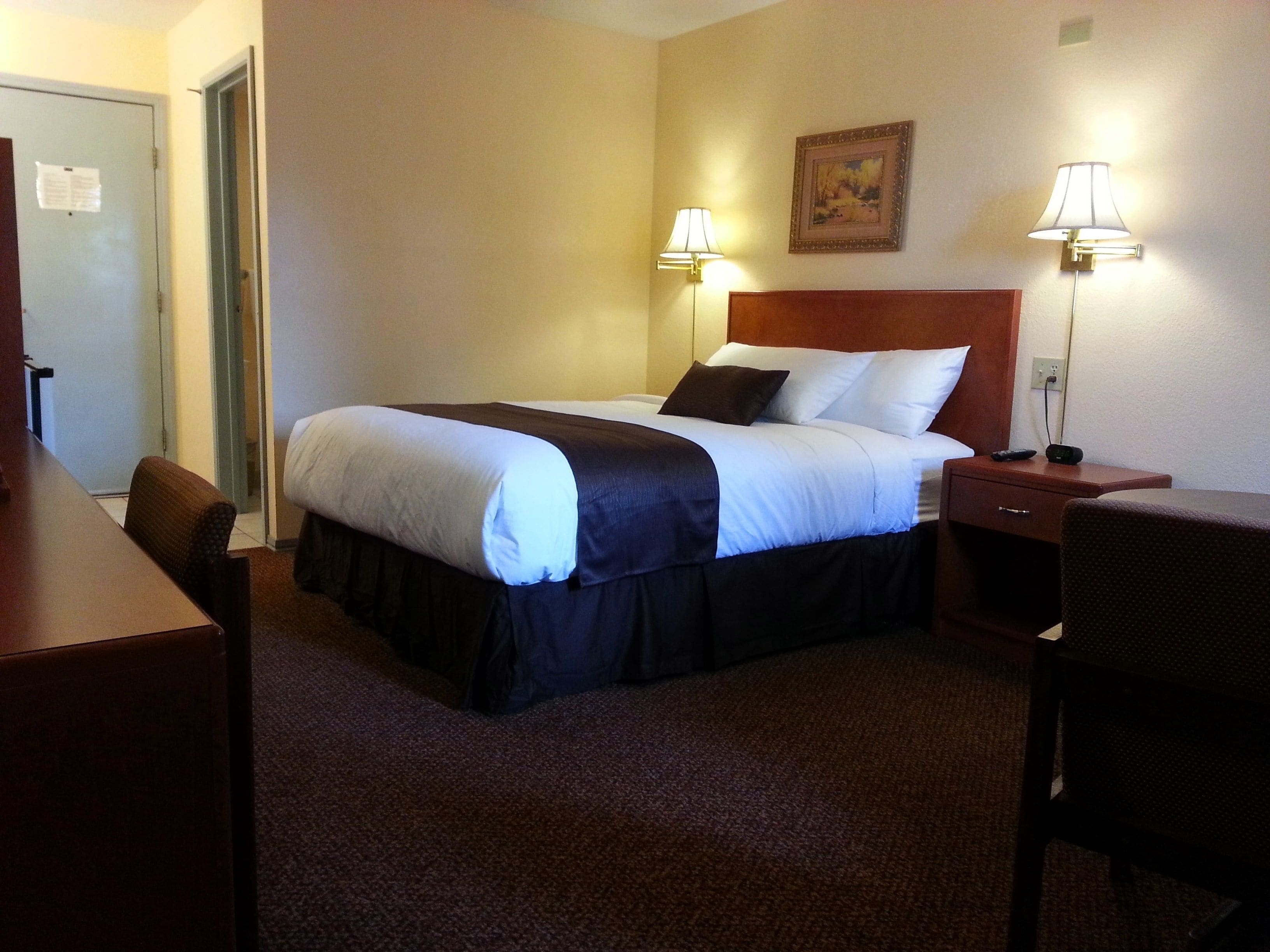 A hotel room with a bed, two bedside lamps, a desk, and a chair.