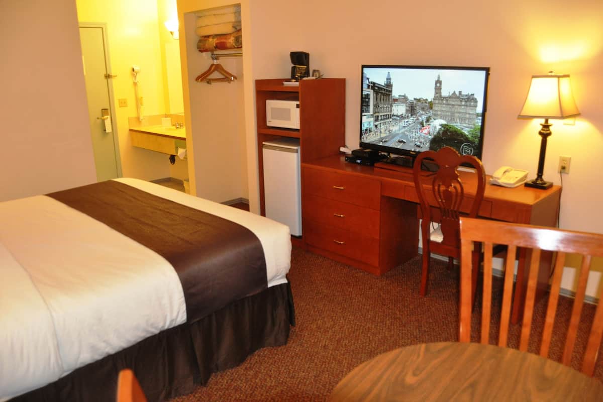 A hotel room with a bed, a desk with a computer, a chair, a lamp, and a television displaying a cityscape.