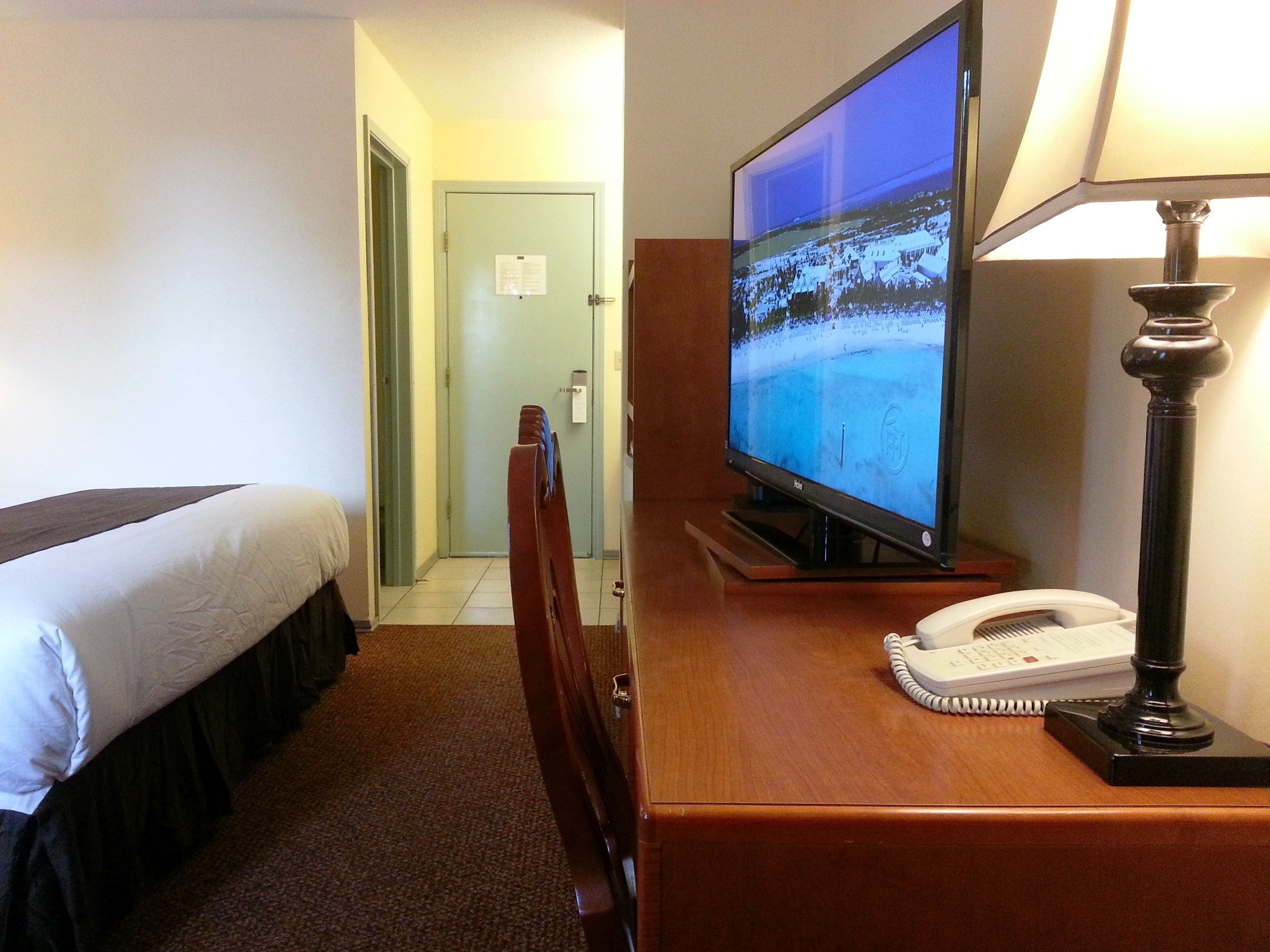A hotel room with a bed, a television displaying a snowy landscape, a desk with a telephone, and a lamp.