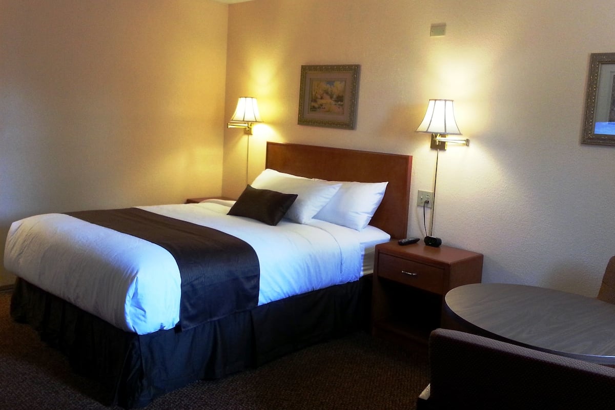 A hotel room with a bed, bedside lamps, a small table, and a chair.