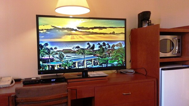 A hotel room with a television displaying a sunset scene, a microwave, a refrigerator, a desk with a chair, and a lamp. - Best Seven Inn (Claresholm)