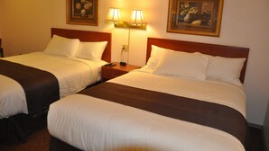 Two twin beds with white linens and dark headboards, a nightstand with a lamp, and two framed floral paintings on the wall. - Best Seven Inn (Claresholm)