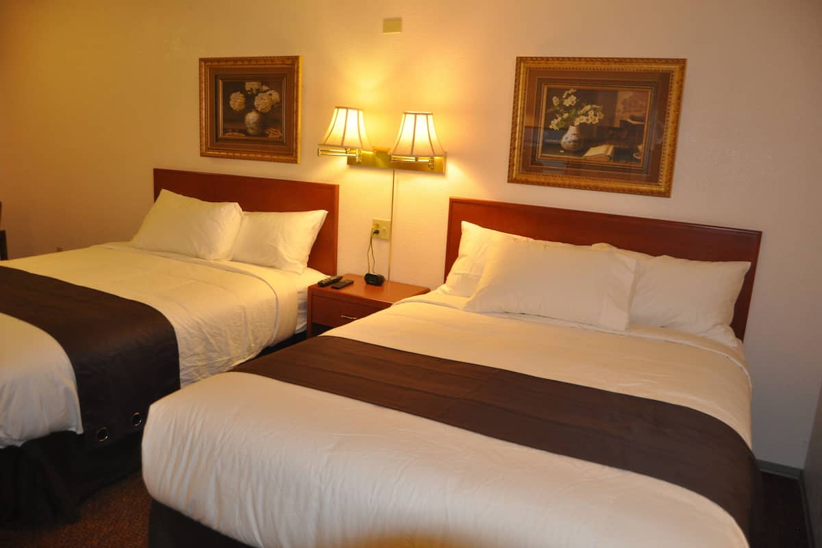 Two twin beds with white linens and dark headboards, a nightstand with a lamp, and two framed floral paintings on the wall.