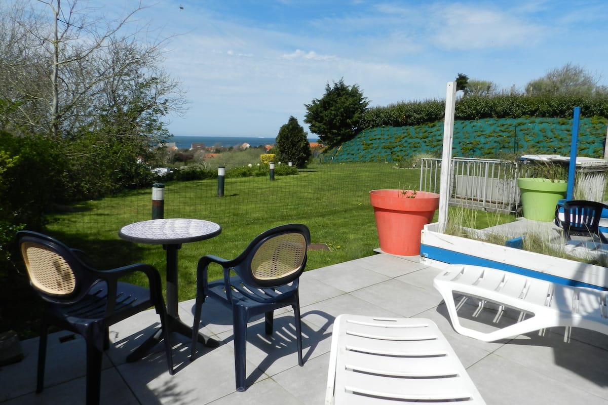 Un patio al aire libre con una mesa, sillas, una maceta grande y vistas al mar.