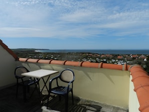Un balcón con mesa y dos sillas, con vistas a un pueblo costero y al mar.