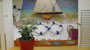 A room with a sailboat mural, life rings, and a potted plant.