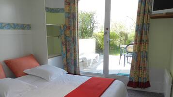 Ein Hotelzimmer mit einem Bett, einer roten Decke, einem Fenster mit Vorhängen und Blick ins Freie.