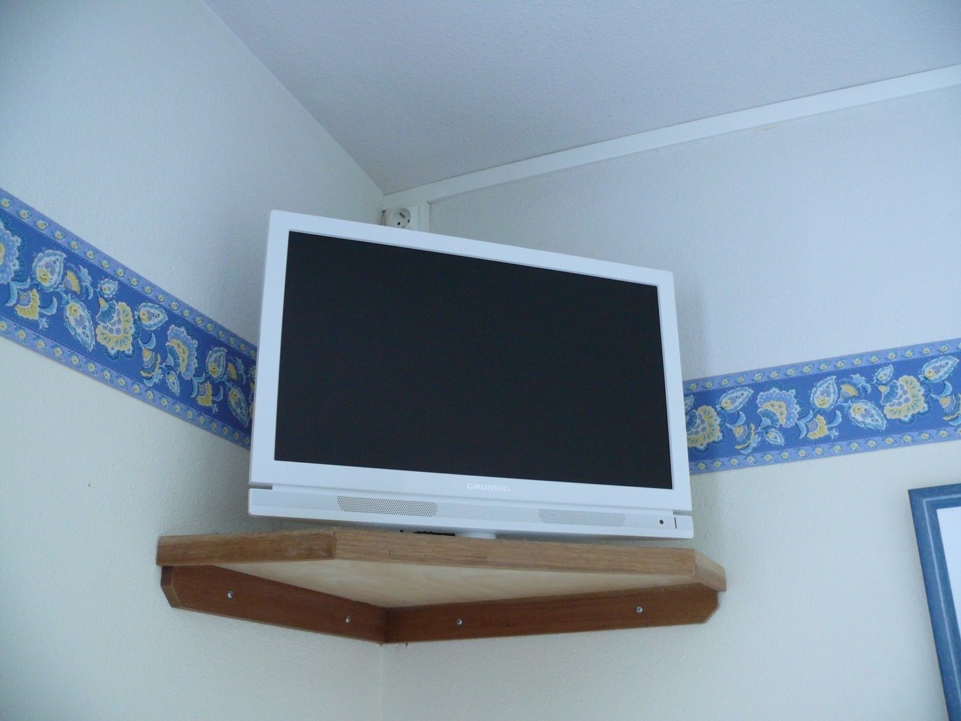Ein Fernseher an einer Holzwandablage in einer Ecke mit dekorativer Tapete.