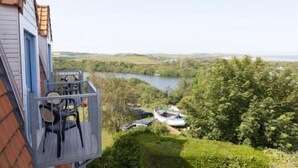 A house with a balcony overlooking a lake, surrounded by greenery.