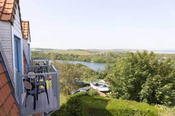 A house with a balcony overlooking a lake, surrounded by greenery.
