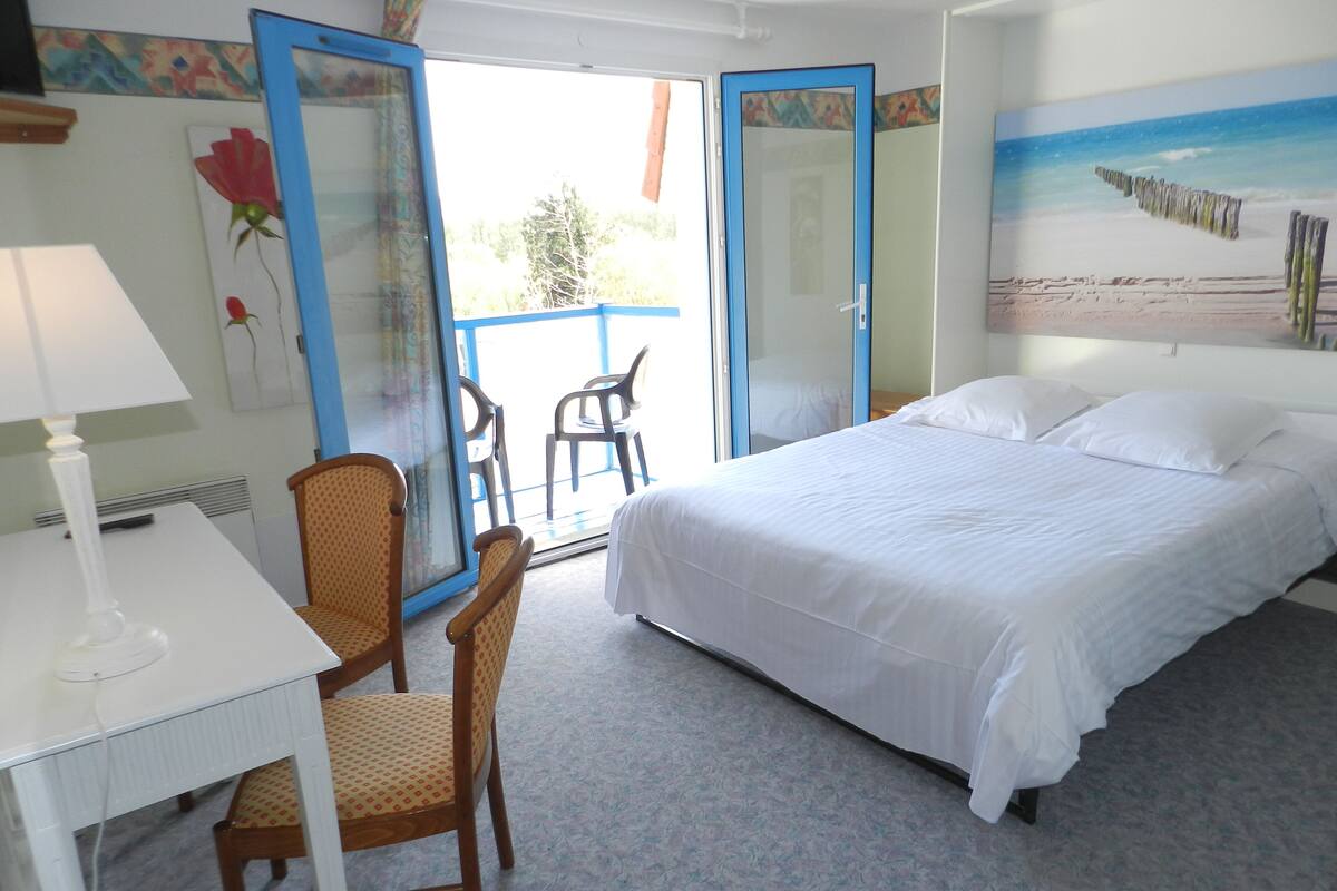 Habitación de hotel con cama, escritorio, silla y balcón con vista a la playa.