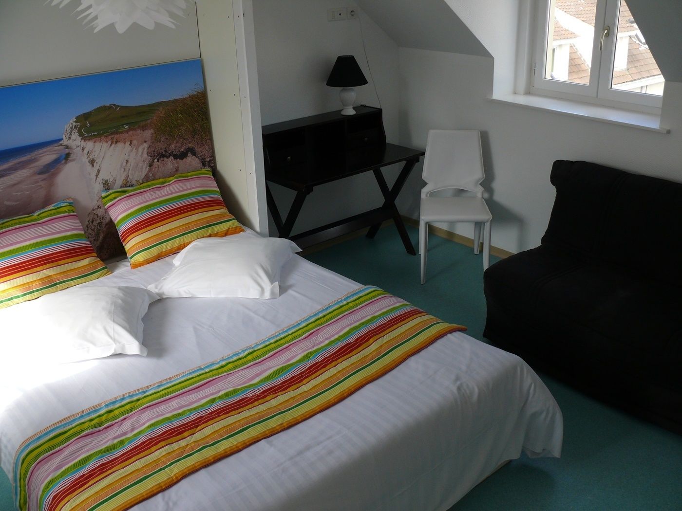 A bedroom with a bed, a desk, a chair, and a window.