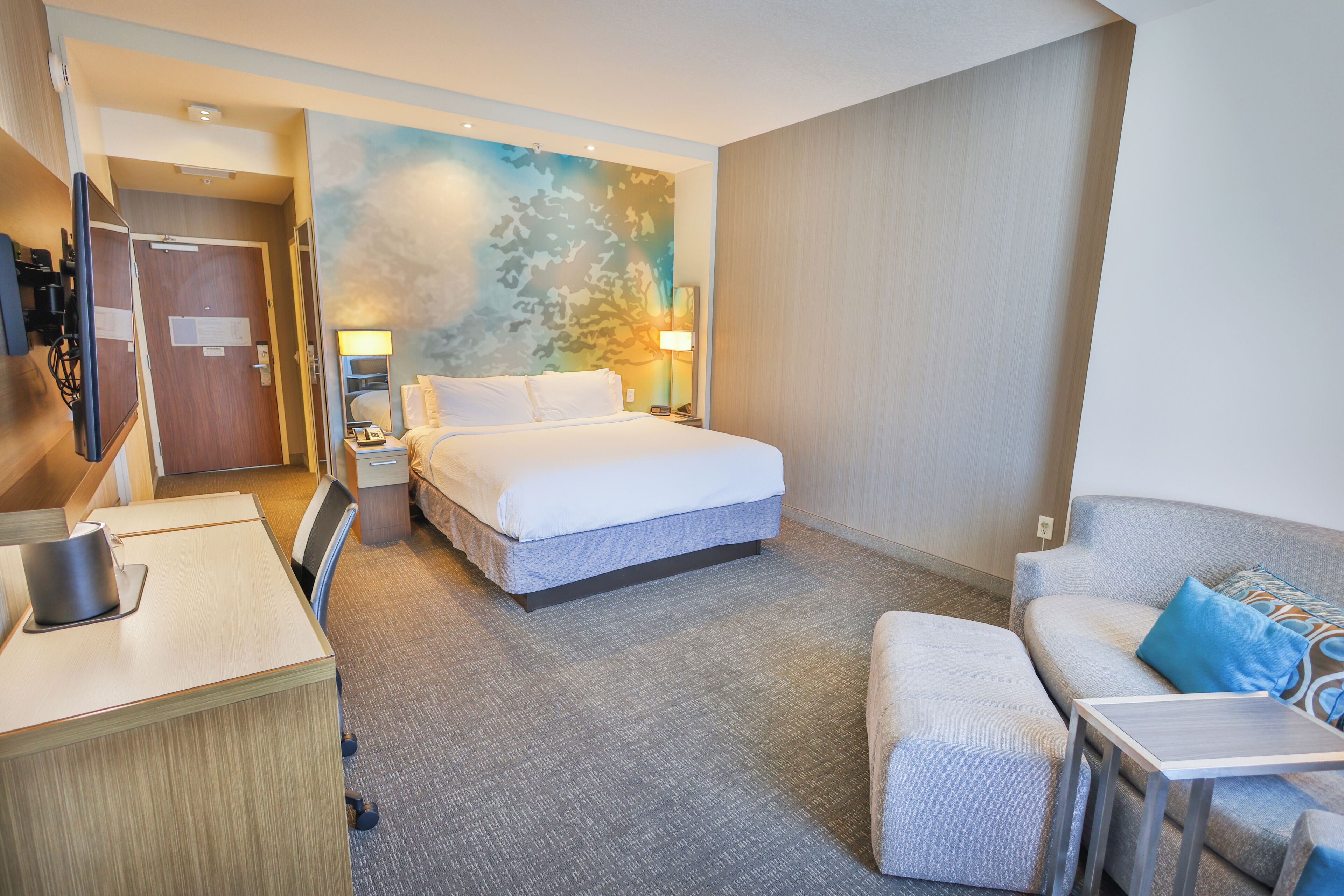 A hotel room with a bed, a desk, a chair, a sofa, and a wall with a camouflage pattern.