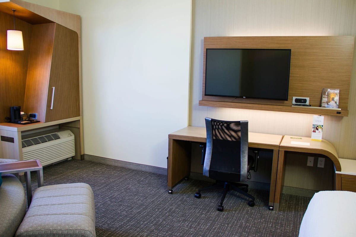 Een hotelkamer met een bureau, stoel, televisie en een kledingkast.