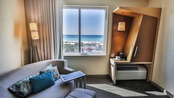 Habitación de hotel con vista a la playa, un sofá con un ordenador portátil, un escritorio con una lámpara y un equipo de aire acondicionado integrado.