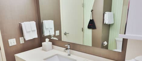 A modern bathroom with a large mirror, a white sink, and a towel rack.