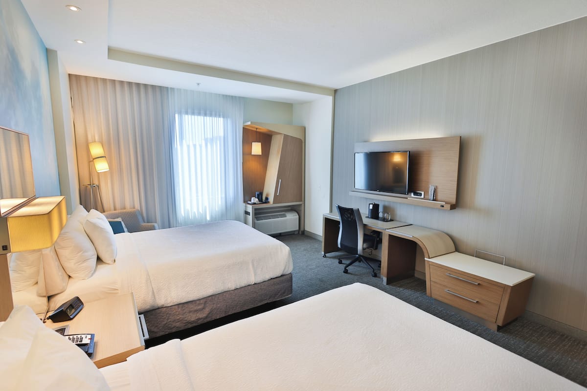 Een hotelkamer met twee bedden, een bureau, een stoel, een televisie en een lamp.