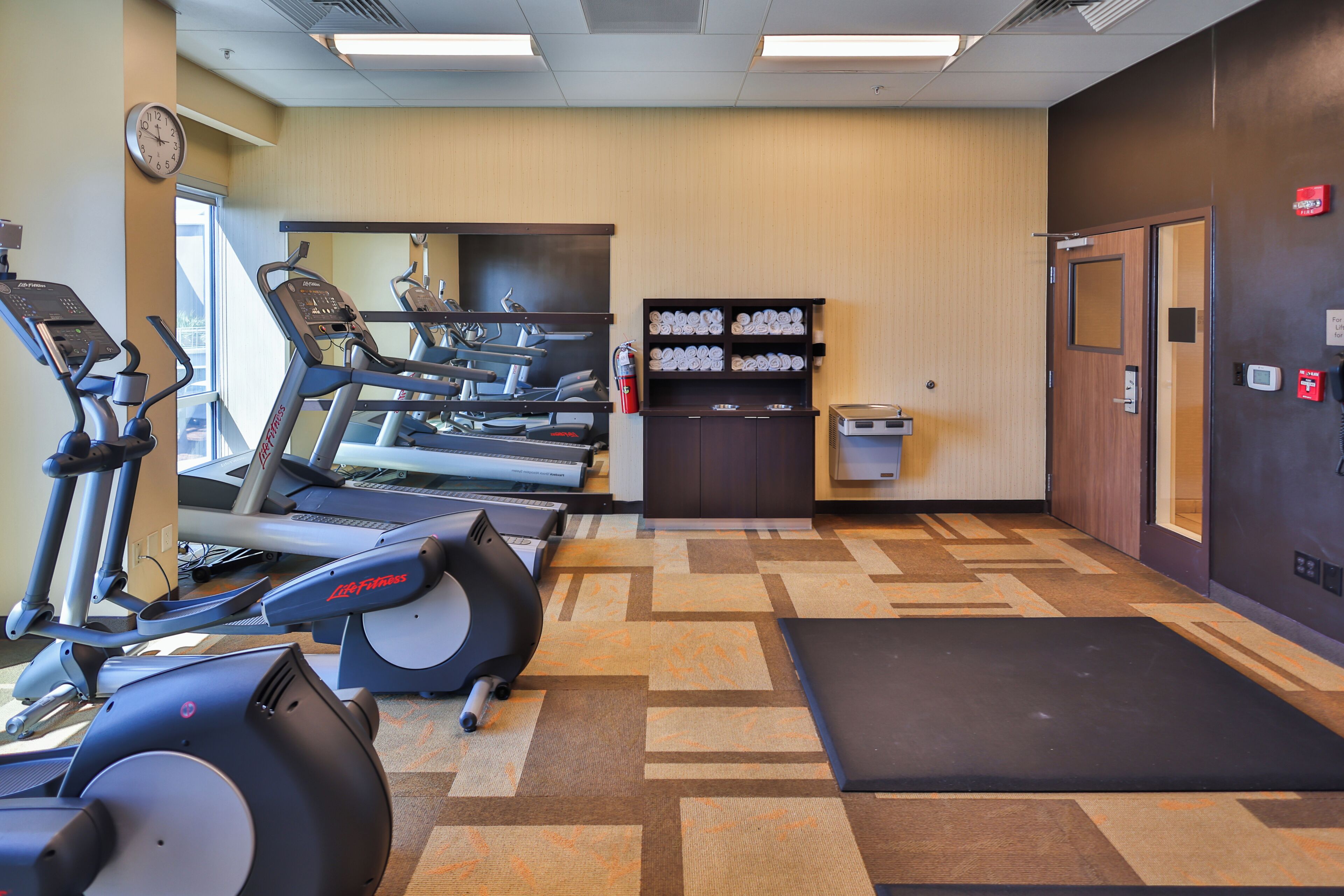A gym with treadmills, elliptical machines, and a mirrored wall.