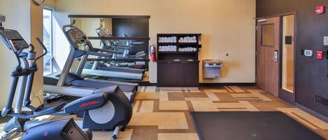 A gym with treadmills, elliptical machines, and a mirrored wall.
