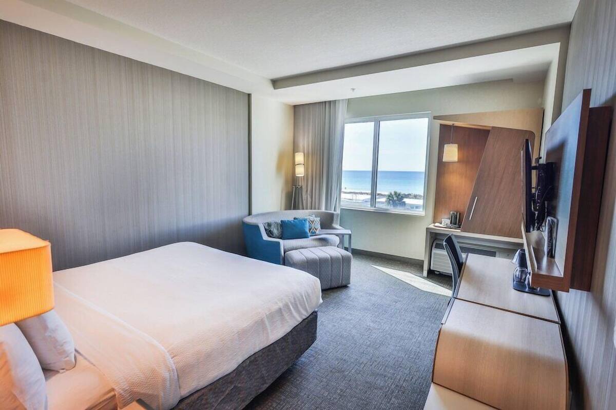Une chambre d’hôtel avec un lit, un bureau, une chaise, une télévision et une fenêtre donnant sur l’océan.