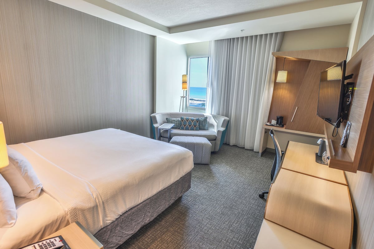 Een hotelkamer met een bed, een bureau, een stoel, een televisie en uitzicht op de oceaan.