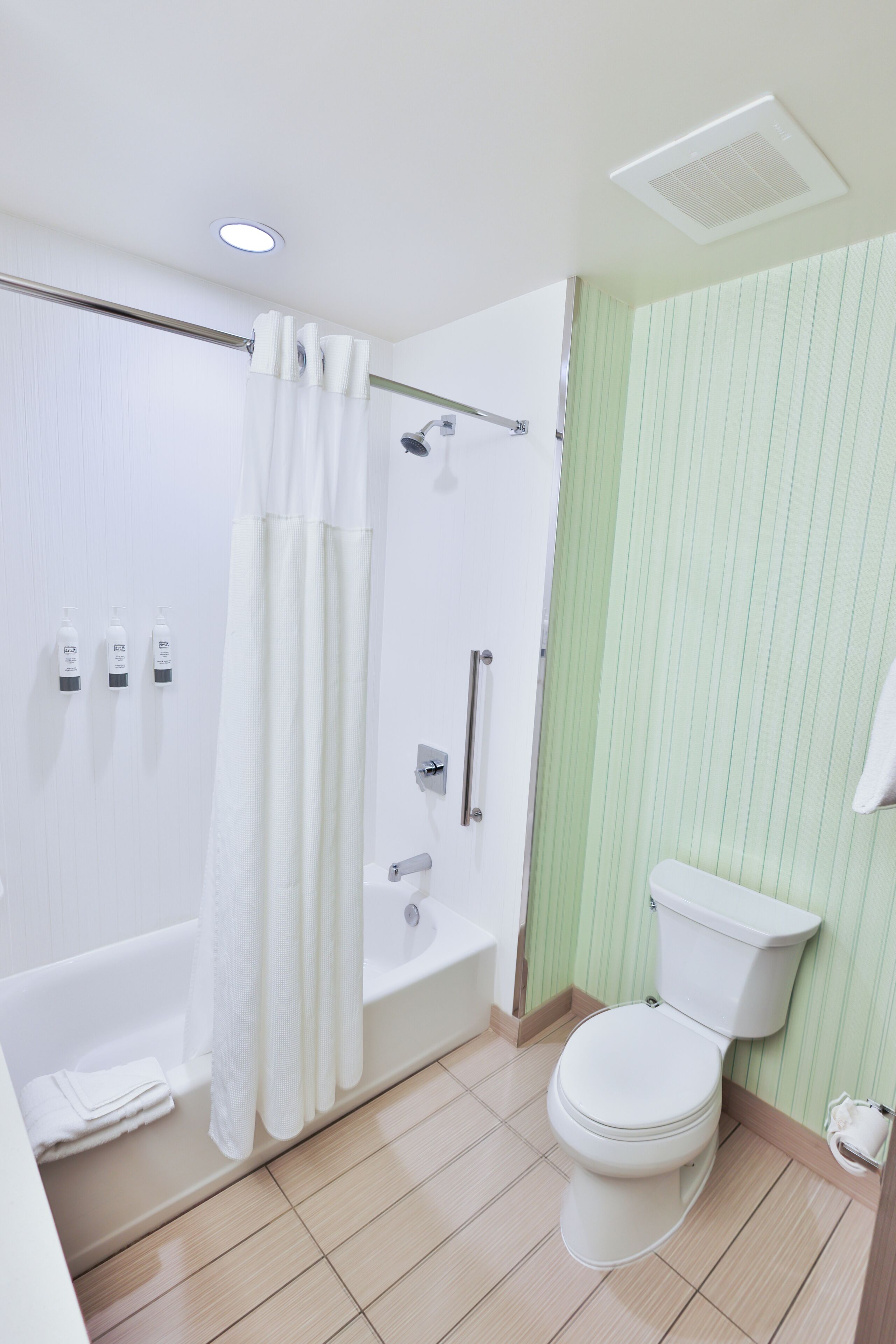 Une salle de bain avec une baignoire, des toilettes, une douche et des murs à rayures vertes.