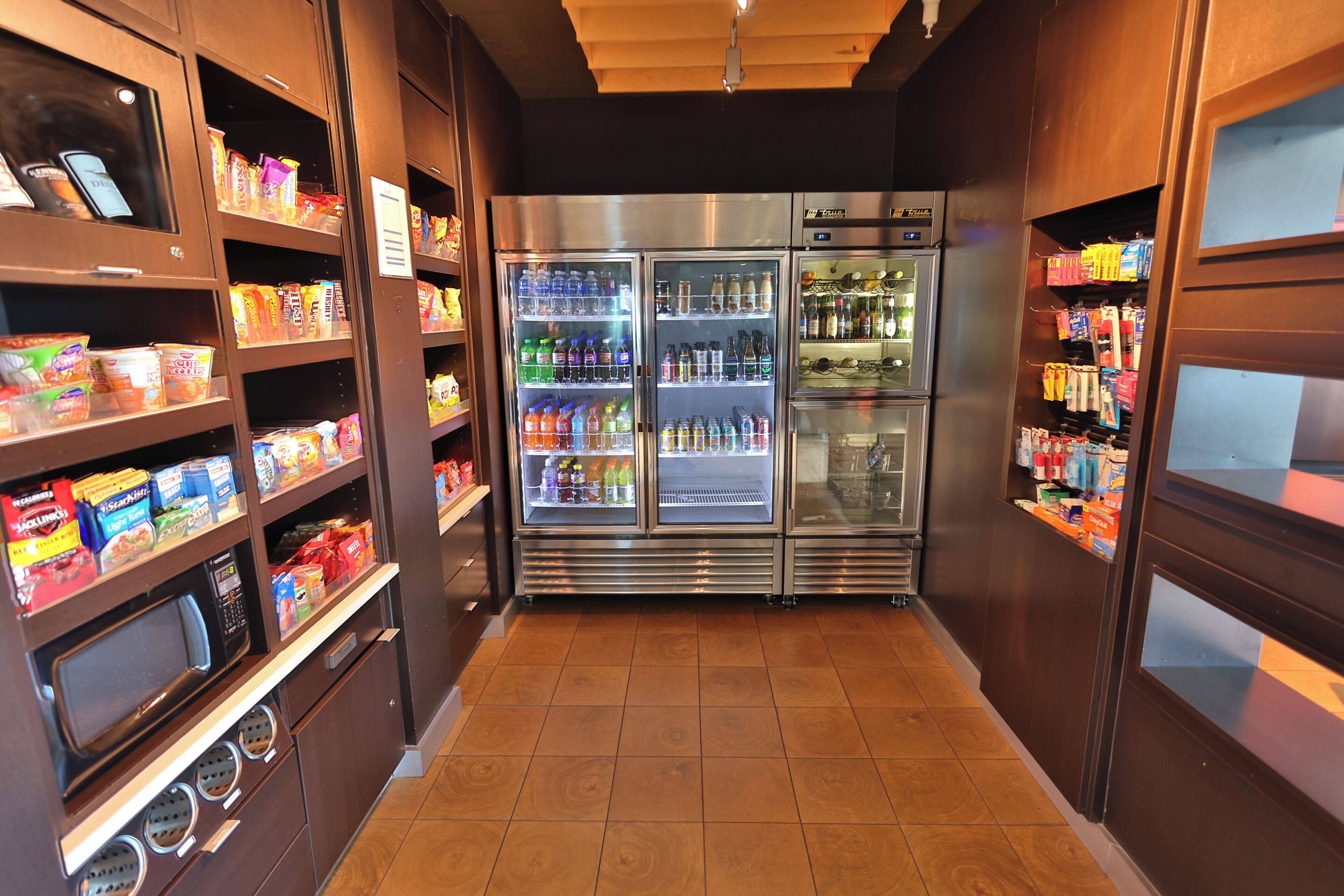 A corridor with vending machines, a microwave, and a refrigerator stocked with beverages and snacks.