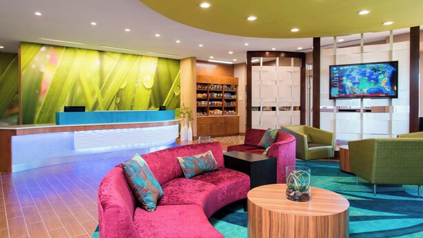 A modern lobby with a curved reception desk, plush seating, a large TV, and a bookshelf.