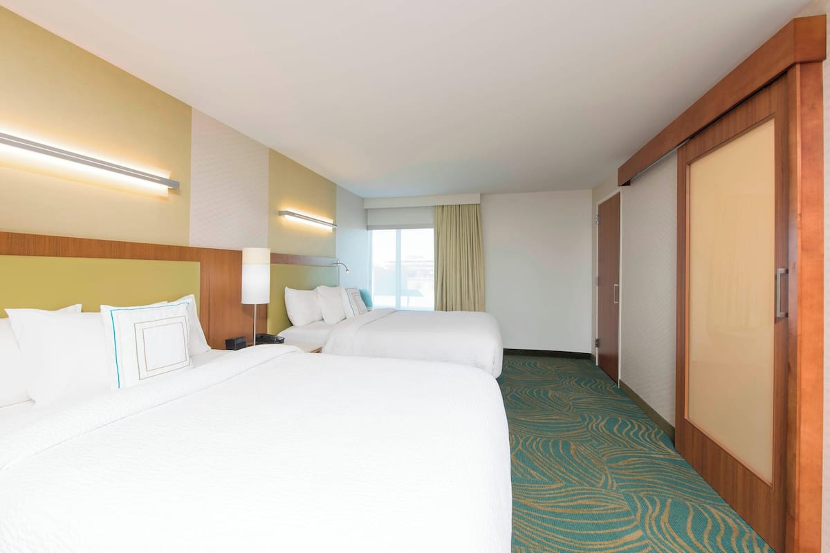 A hotel room with two beds, a large window with curtains, and a wooden wardrobe.