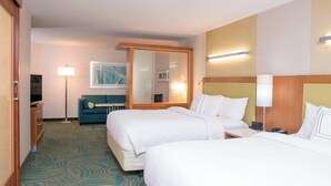 A hotel room with two beds, a desk, a chair, a sofa, a TV, and a mirror.
