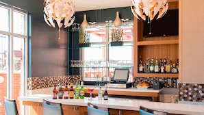 A bar area with a counter, bar stools, a cash register, shelves with bottles, and a television.