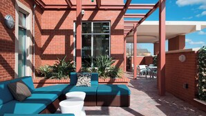 An outdoor patio with a brick wall, a glass door, and a seating area with a blue sofa and white table.