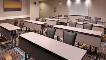 A conference room with multiple tables and chairs, a clock, a whiteboard, and a projector screen.