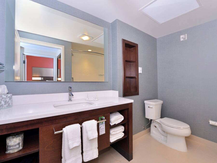 A modern bathroom with a large mirror, a white sink, a toilet, and a wooden vanity with towels.