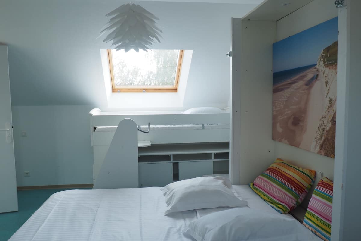 A bedroom with a bunk bed, a desk, a window, and a beach-themed wall art.