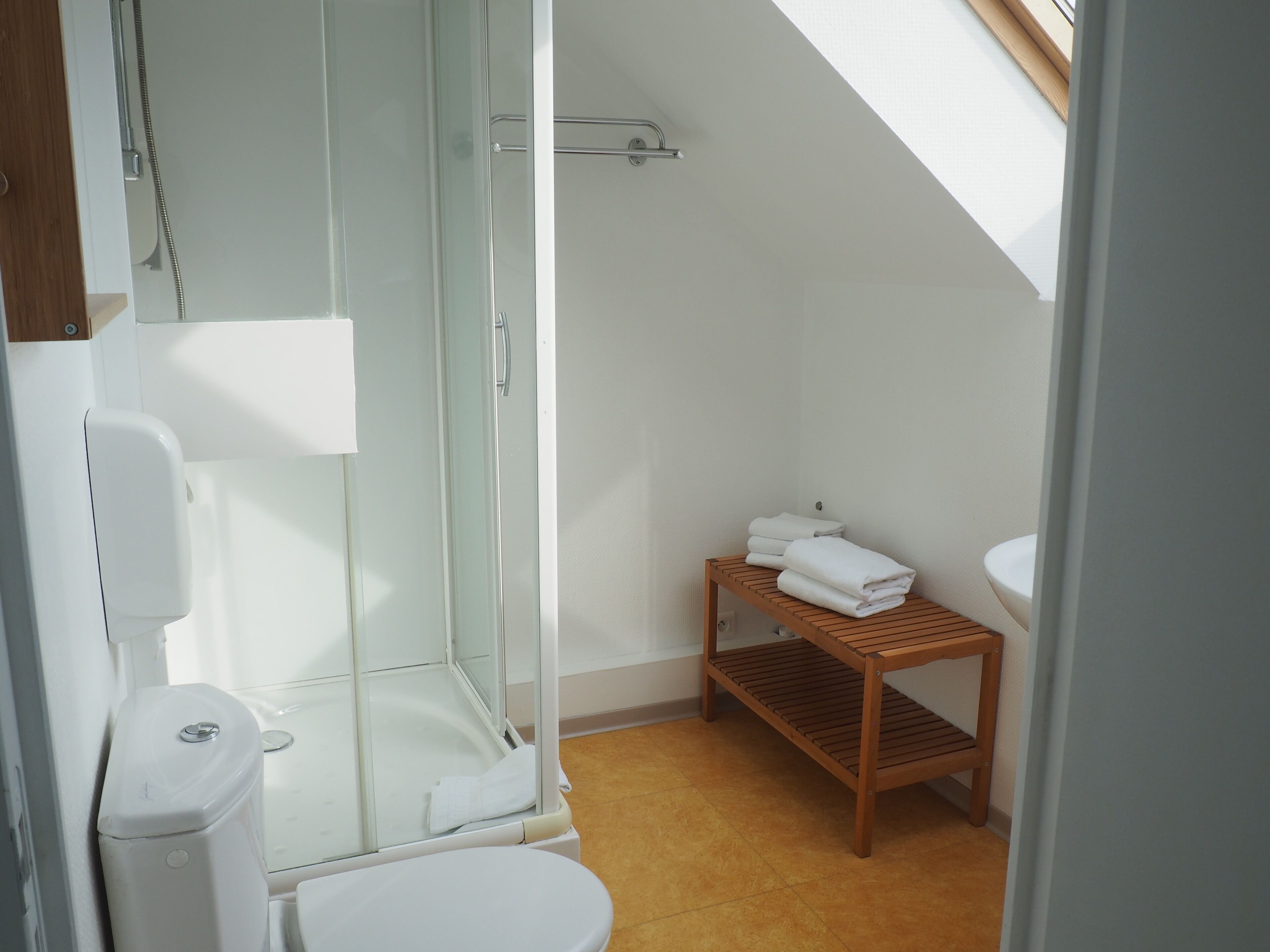 A modern bathroom with a glass shower enclosure, a wooden shelf with towels, and a white toilet.