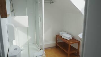A modern bathroom with a glass shower enclosure, a wooden shelf with towels, and a white toilet.