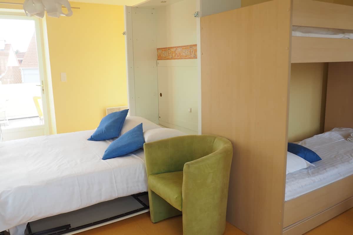 A room with a bunk bed, a green chair, and a bed with blue pillows.