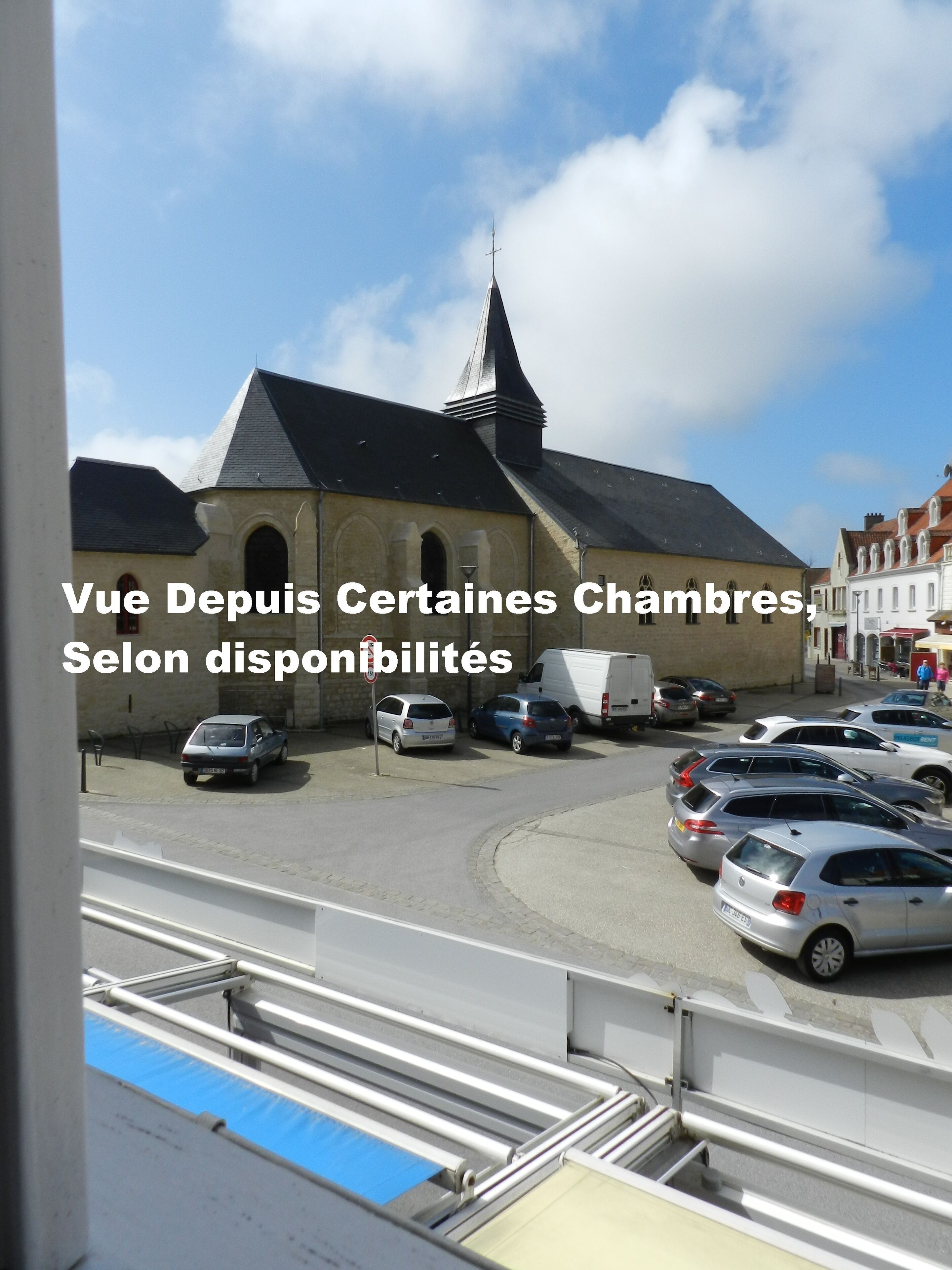 A church with a pointed steeple and a parking lot in front.