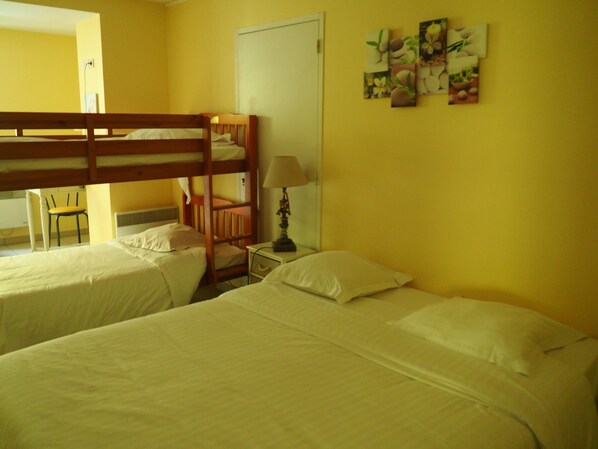 A room with two beds, a chair, a nightstand with a lamp, and a door.