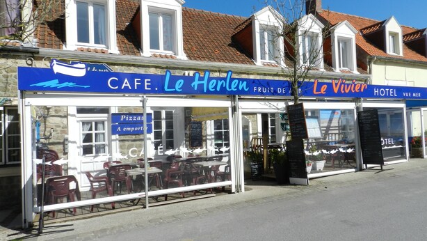 Um café com mesas ao ar livre, um letreiro com 'Le Herlen' e um 'Hotel Vue Mer' na rua.