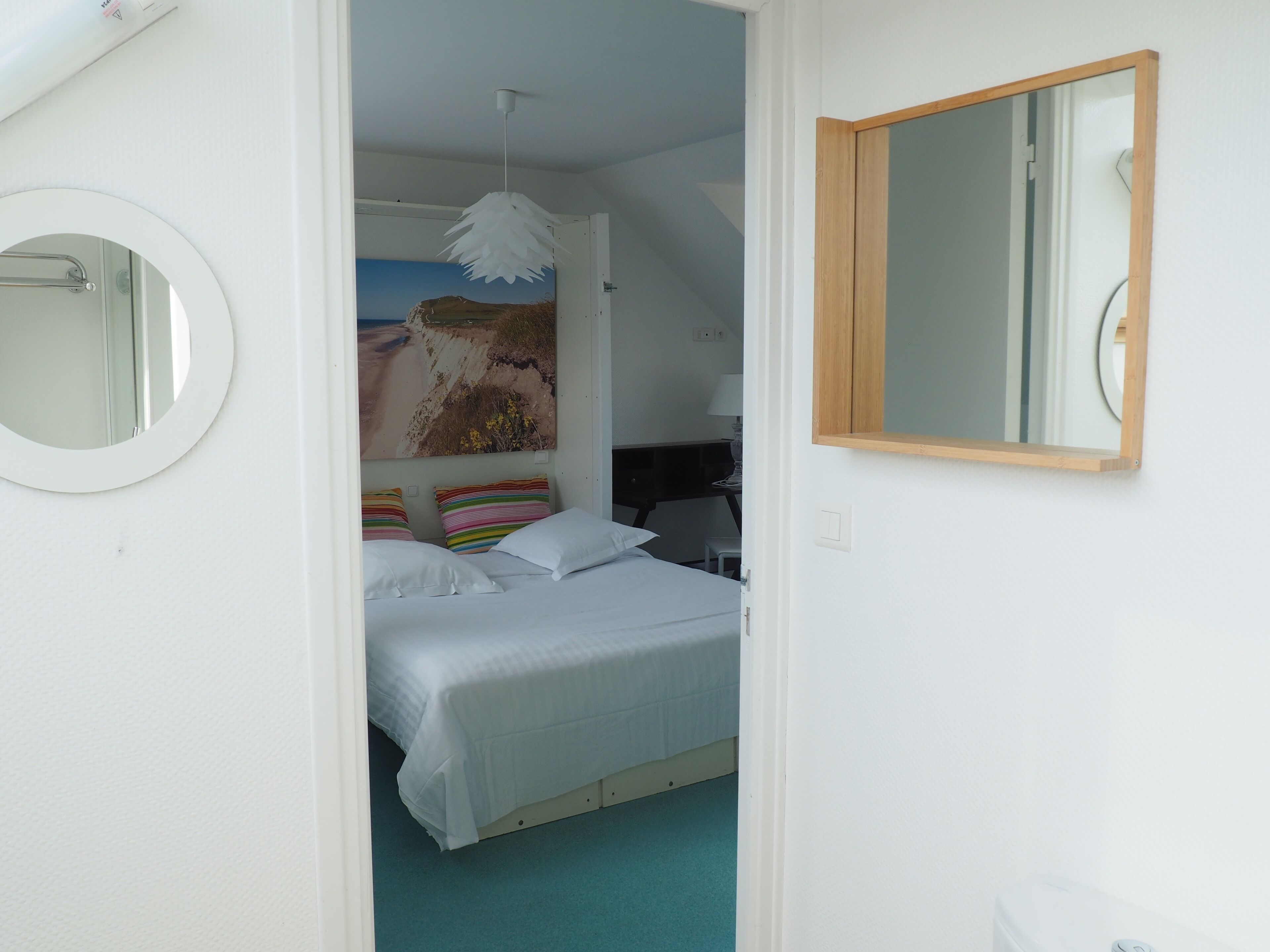 Un dormitorio con cama, un espejo redondo y una pintura de una escena de playa.
