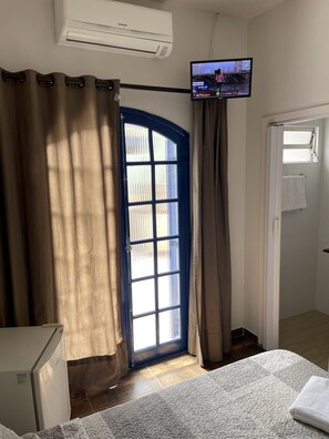 A hotel room with a bed, a TV mounted on the wall, a window with curtains, and a door. - Villa Di Verona (Guarujá)